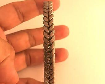 May include: A silver bracelet with a braided design. The bracelet is made of small, interlocking links that create a woven pattern.