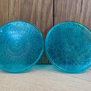Könnte beinhalten: Zwei runde, blaue, dekorative Untersetzer mit komplizierten Designs. Ein Untersetzer zeigt ein kreisförmiges Mandala-Muster, während der andere ein florales Design hat.