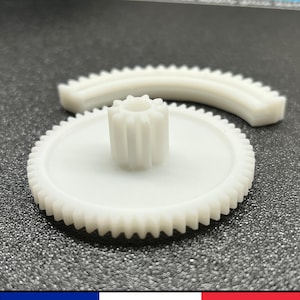 Peut inclure: Deux engrenages en plastique blanc, l'un plus grand que l'autre, avec des dents sur les bords. Le plus petit engrenage est fixé au centre du plus grand.
