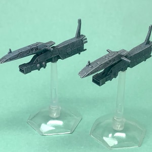 May include: Two gray, detailed, miniature spaceships on clear plastic stands. The spaceships have a futuristic design with sharp angles and a sleek, metallic finish.