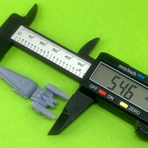 May include: A gray spaceship model measuring 5.46 inches in length, being measured with a digital caliper.