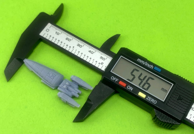 May include: A gray spaceship model measuring 5.46 inches in length, being measured with a digital caliper.
