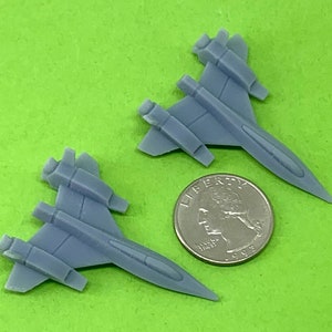 May include: Two gray plastic model airplanes, each with a wingspan of approximately 2.5 inches. The airplanes are sitting on a green surface next to a US quarter.