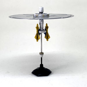 May include: A silver model of a rotating radar dish with two yellow and blue wings on a black base.