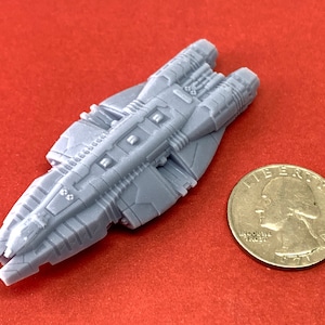 May include: A gray, detailed, miniature spaceship model with a long, pointed nose and two engines at the rear. The model is about the size of a US quarter.