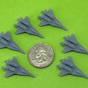 May include: Six gray plastic model fighter jets arranged in a circle around a US quarter dollar coin. The jets have three missiles each.