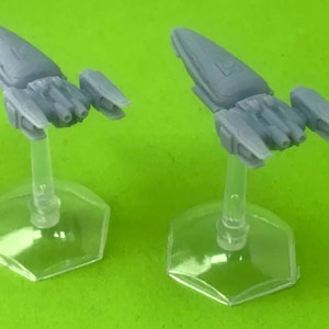 May include: Two gray miniature spaceships on clear plastic bases. The spaceships have a sleek, futuristic design with pointed noses and wings.