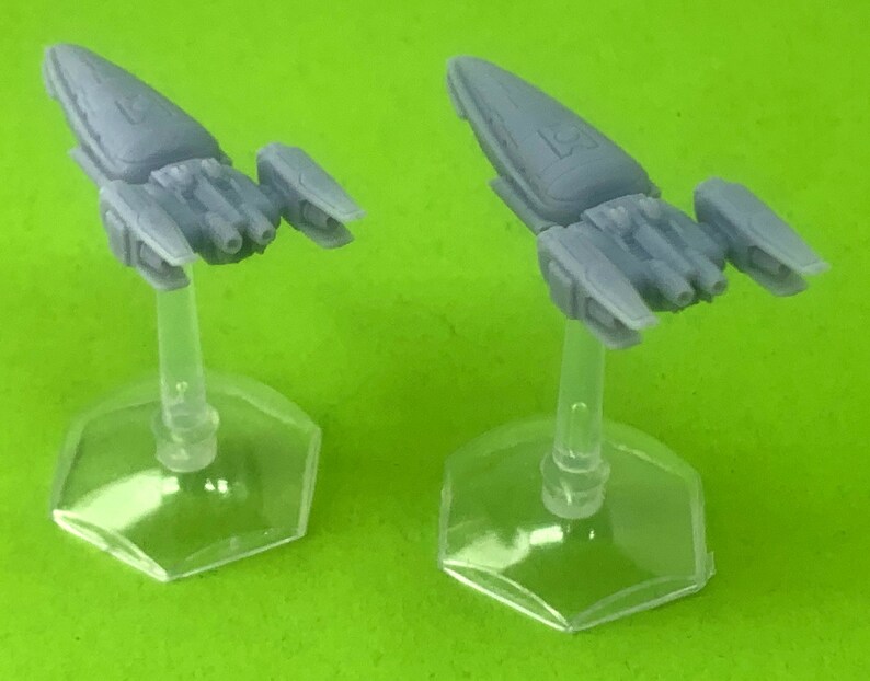 May include: Two gray miniature spaceships on clear plastic bases. The spaceships have a sleek, futuristic design with pointed noses and wings.