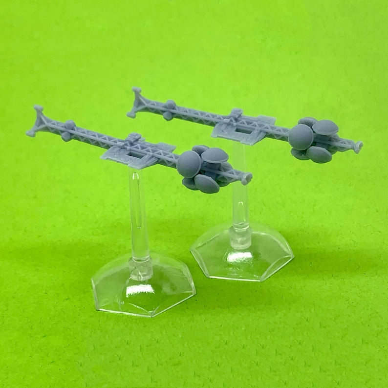 May include: Two gray, detailed, miniature spaceships with multiple round, disc-like features on the ends of each ship. The spaceships are on clear plastic stands.