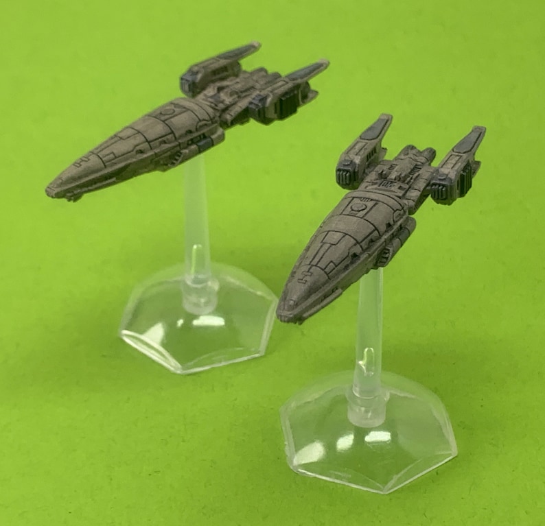 May include: Two miniature spaceships painted in a camouflage pattern, each on a clear plastic stand. The spaceships are detailed with a variety of panels and hatches.