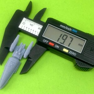 May include: A gray plastic spaceship model being measured with a digital caliper. The caliper reads 19.7 mm.