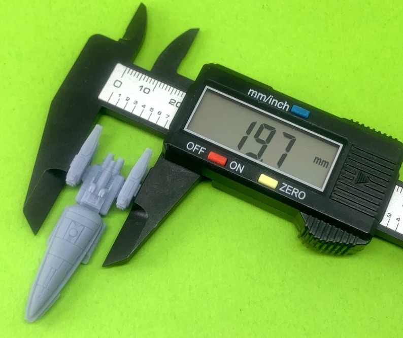 May include: A gray plastic spaceship model being measured with a digital caliper. The caliper reads 19.7 mm.
