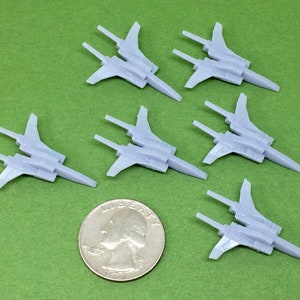 May include: Six gray plastic model fighter jets on a green surface. The jets have pointed noses, swept wings, and vertical stabilizers. A US quarter is included for scale.