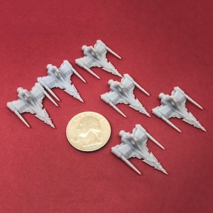 May include: Six gray plastic miniature spaceships with pointed wings and a cockpit. The spaceships are arranged in a semi-circle on a red surface. A US quarter is included for scale.