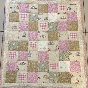 May include: A pink and white patchwork quilt with a checkered heart design. The quilt is made up of various squares with different patterns and colours. The quilt is perfect for a baby's nursery or a child's bedroom.