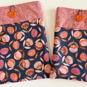 May include: Two fabric pouches with a pink and white speckled fabric top and a dark blue floral print bottom. The pouches have a button closure and a black cord.
