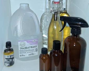 May include: A collection of glass and amber-colored bottles and a large plastic jug. The bottles are labeled with "Vinegar", "Alcohol", and "Castile Soap". The amber bottles are labeled with "2 oz", "4 oz", and "16 oz". A jug of distilled water is also present.