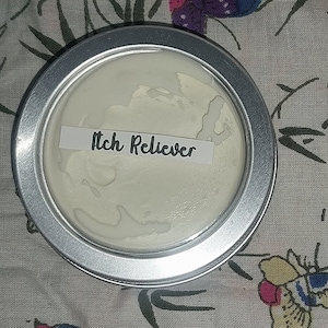 Puede incluir: Una lata plateada con una etiqueta blanca que dice "Itch Reliever". La lata está llena de una crema blanca.