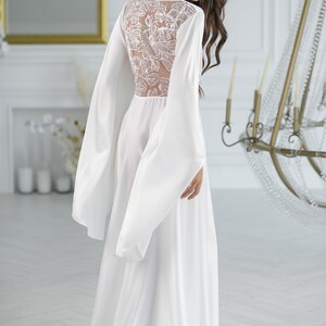 May include: A white satin robe with long sleeves and a floral lace back panel. The robe has a flowing silhouette and a relaxed fit.