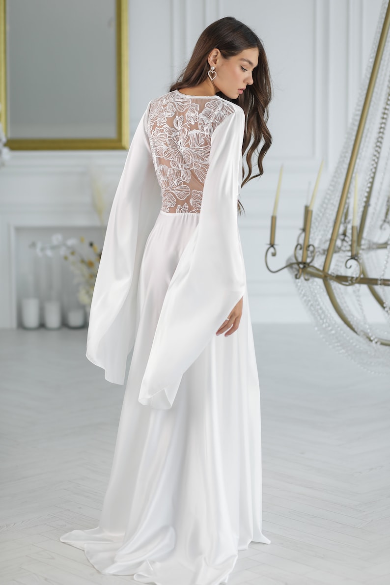 May include: A white satin robe with long sleeves and a floral lace back panel. The robe has a flowing silhouette and a relaxed fit.