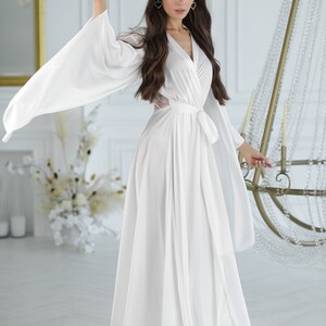 May include: A white satin robe with long sleeves and a tie belt. The robe has a V-neckline and a lace detail on the back.