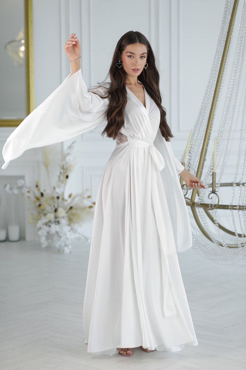 May include: A white satin robe with long sleeves and a tie belt. The robe has a V-neckline and a lace detail on the back.