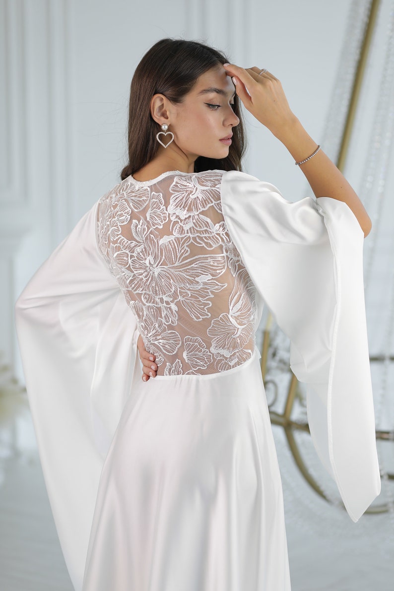 May include: A white satin dress with a lace back and long, flowing sleeves. The dress has a simple, elegant design and is perfect for a special occasion.