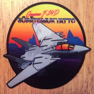Puede incluir: Un parche redondo, negro y blanco con un avión de combate F-14D Tomcat gris volando sobre un paisaje de puesta de sol. El texto "Grumman F-14D SUPATOMUKYATTO" está impreso en una fuente retro de los años 80.