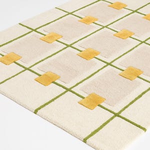 May include: Cream-colored rectangular rug with a geometric pattern. The design features a grid of green lines, beige squares, and yellow diamond accents. The rug has a textured surface and a modern aesthetic.
