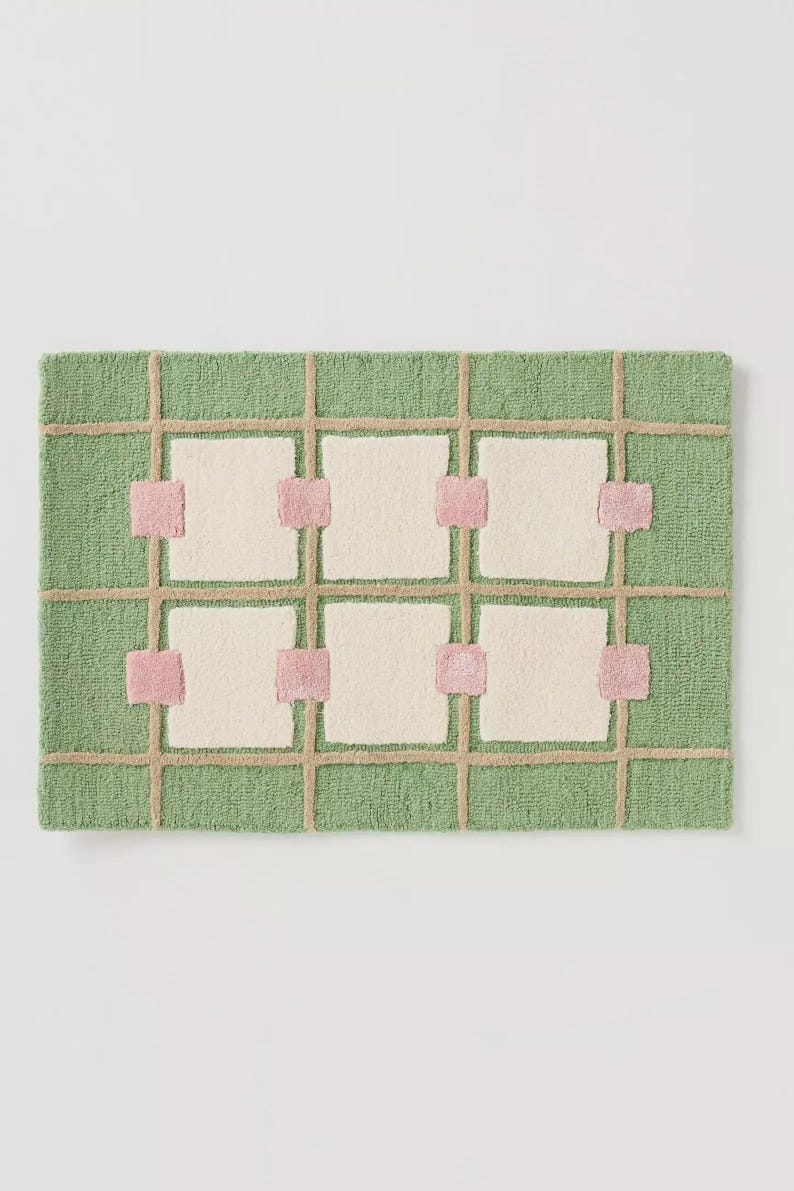 Puede incluir: Alfombra rectangular con fondo verde y dise&ntilde;o de cuadr&iacute;cula. Las l&iacute;neas de la cuadr&iacute;cula son de color beige y los cuadrados est&aacute;n rellenos de blanco roto. Cuadrados rosas acent&uacute;an las intersecciones de la cuadr&iacute;cula. La alfombra tiene un aspecto texturizado y tejido.