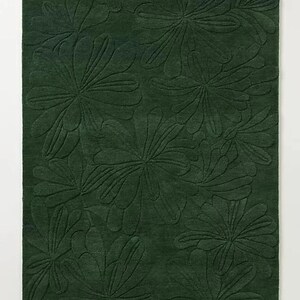 May include: A dark green rug with a repeating floral pattern. The design features large, stylized flowers with detailed leaf patterns, creating a textured, dimensional effect. The rug's color is a deep, forest green.