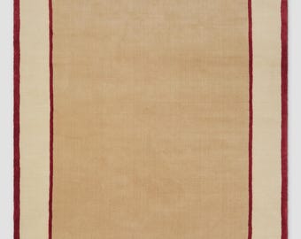 May include: A rectangular area rug featuring a solid tan center panel, a wide cream-colored border, and a thin, deep red accent line separating the two sections, finished with a matching deep red edge along the entire outer perimeter.