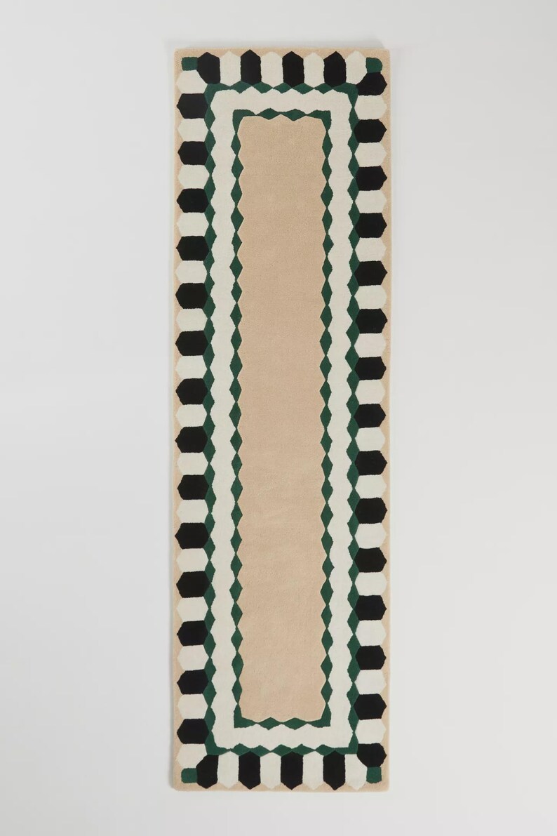 May include: A rectangular rug with a beige center and a geometric border. The border features black, white, and green shapes. The rug's design is symmetrical and modern, suitable for various interior styles.