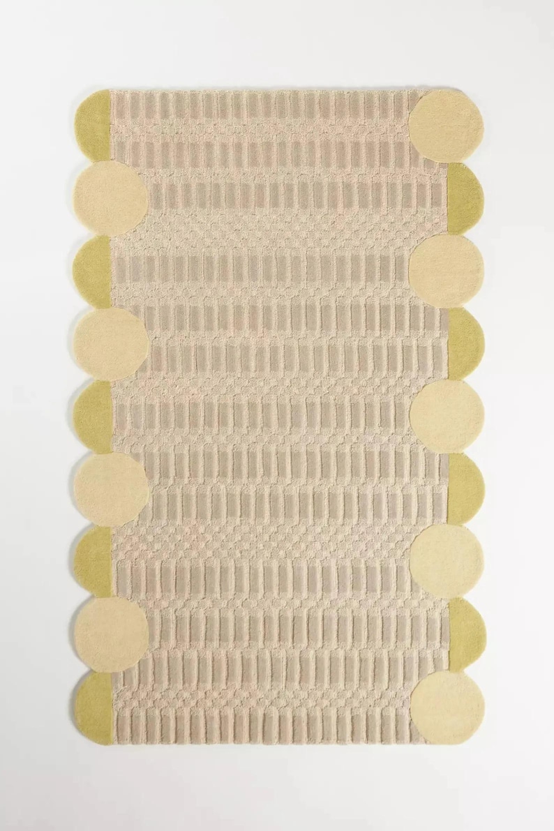 Pu&ograve; includere: Un tappeto rettangolare con un motivo beige strutturato. Il tappeto &egrave; bordato da cerchi beige e semicerchi verde tenue alternati. Il design del tappeto presenta linee verticali e orizzontali, creando un motivo geometrico.