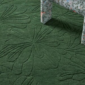 May include: A dark green rug with a raised floral pattern. The rug's texture is visible, and a chair with a floral pattern is partially visible in the background.