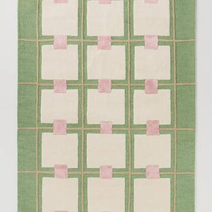 Puede incluir: Una alfombra rectangular con fondo verde y un patr&oacute;n de cuadr&iacute;cula. La cuadr&iacute;cula est&aacute; hecha de l&iacute;neas beige, rect&aacute;ngulos blanquecinos y cuadrados rosas. La alfombra es un revestimiento decorativo para el suelo.
