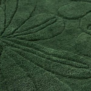 May include: Close-up of a dark green rug with a floral leaf pattern. The design is embossed, creating a textured surface. The rug's color is a deep, rich shade of green, suitable for home decor.