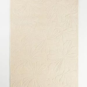 Puede incluir: Una alfombra rectangular de color crema con un patr&oacute;n floral repetitivo. Las flores est&aacute;n estilizadas con m&uacute;ltiples p&eacute;talos y est&aacute;n en relieve, creando un efecto texturizado. La alfombra est&aacute; sobre un fondo blanco.