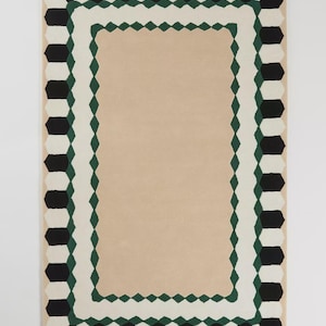 May include: Rectangular rug with a beige center and a patterned border. The border features alternating black and white geometric shapes, with a green diamond pattern in between. The rug is designed for home decor.
