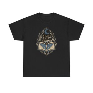 Könnte beinhalten: Ein schwarzes T-Shirt mit einem Grafikdruck eines aufgeschlagenen Buches, auf dessen Seiten ein blauer Nachtfalter ruht. Über dem Buch befinden sich eine Mondsichel und der Text "NIGHT SHIFT READER" in Serifenschrift, umrahmt von feinen Ranken.