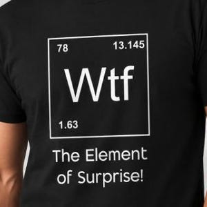 Könnte beinhalten: Ein schwarzes T-Shirt mit einer weißen Grafik, die wie ein Elementfeld aus dem Periodensystem gestaltet ist. Das Feld enthält den Text Wtf, die Zahl 78, die Zahl 13.145 und die Zahl 1.63. Unter dem Feld steht der Text The Element of Surprise!
