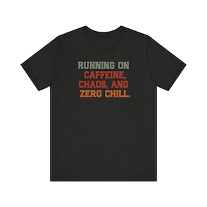 Könnte beinhalten: Schwarzes T-Shirt mit dem Text "RUNNING ON CAFFEINE, CHAOS, AND ZERO CHILL" in Grün, Rot und Orange. Der Text hat einen Vintage-Stil.