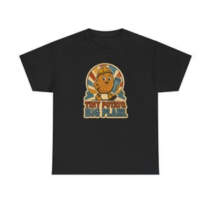Könnte beinhalten: Ein schwarzes T-Shirt mit einer Grafik einer Cartoon-Kartoffel, die einen gelben Bauhelm trägt und einen blauen, gerollten Bauplan hält. Hinter der Kartoffel befindet sich ein Retro-Sonnenstrahlen-Design. Der Text darunter lautet "TINY POTATO. BIG PLANS."