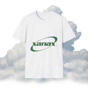 May include: White t-shirt with a green "xanax" logo. The logo is in a stylized font, with the word inside a curved design. The shirt is made of a soft material and has a crew neck.
