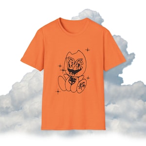 May include: Orange t-shirt featuring a black cartoon graphic. The graphic depicts a stylized creature with a large head, open mouth, and small body. The design includes stars and other small details.