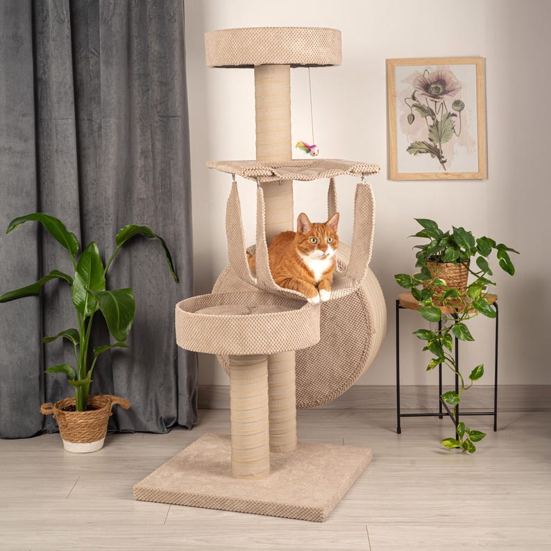 May include: Beige cat tree with multiple levels, including a hanging bed, a round platform, and a top perch. A ginger cat is sitting in the hanging bed.