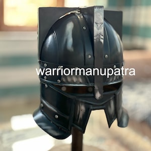 Peut inclure: Un casque noir avec une visière en métal et une barre métallique verticale sur le dessus. Le casque a une surface texturée et est décoré de rivets. Le casque est sur un support en bois.