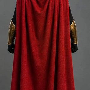 May include: A costume featuring a long red cape, a gold-colored helmet with a central crest, gold-colored forearm bracers, and gold-trimmed black boots. The text WARRIOR MANIPATARA is visible on the upper back of the red cape in white lettering.