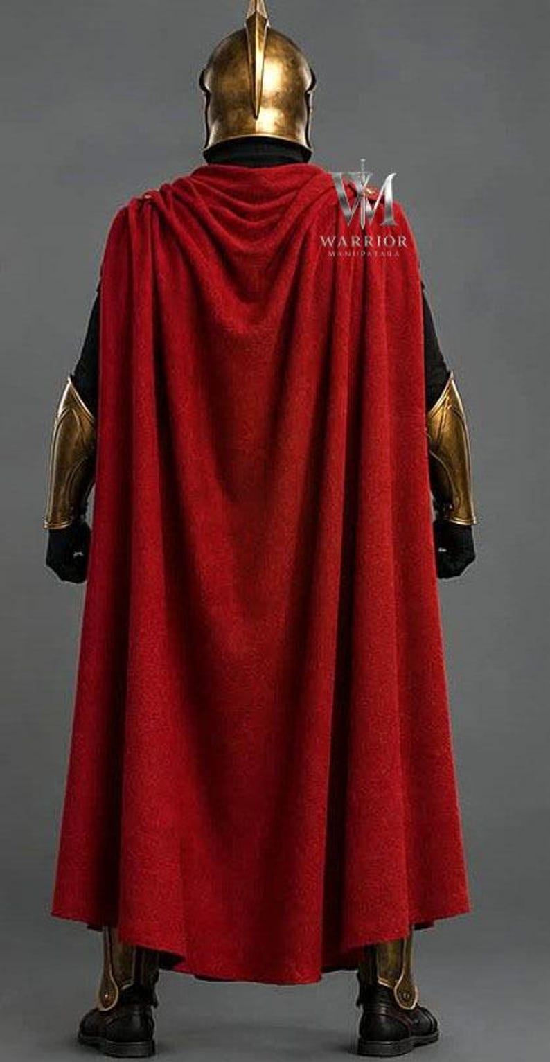 May include: A costume featuring a long red cape, a gold-colored helmet with a central crest, gold-colored forearm bracers, and gold-trimmed black boots. The text WARRIOR MANIPATARA is visible on the upper back of the red cape in white lettering.