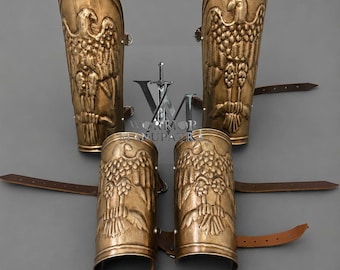 Può includere: Un set di quattro schinieri e bracciali in metallo color ottone con disegni di aquile in rilievo. Ogni pezzo include cinturini in pelle marrone per il fissaggio. Gli articoli sono disposti simmetricamente, con due pezzi più grandi sopra due pezzi più piccoli.